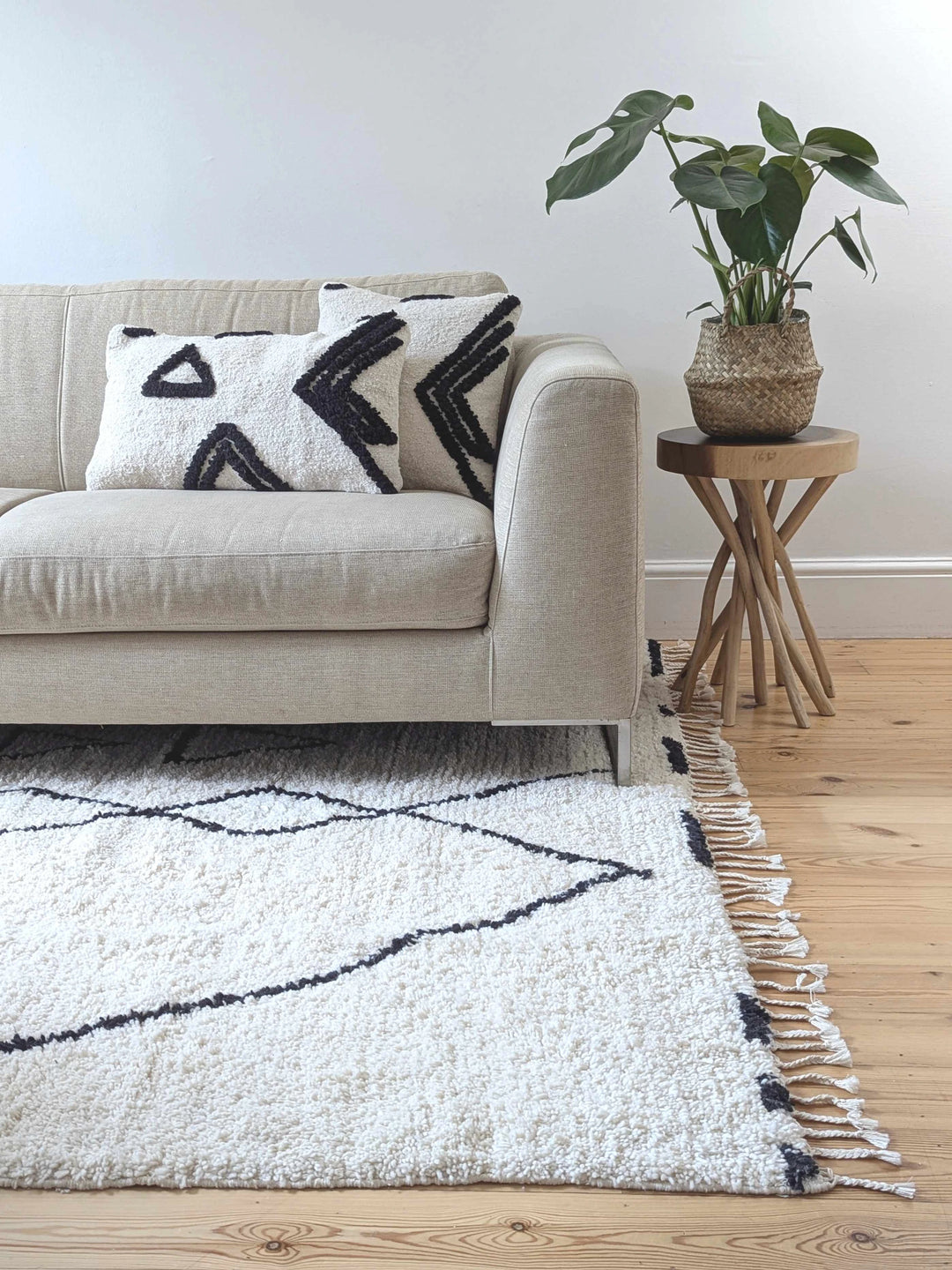 Black and cream natural wool berber rug with abstract design next to sofa and plant 